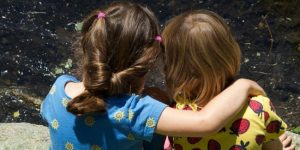 two young girls sit hugged